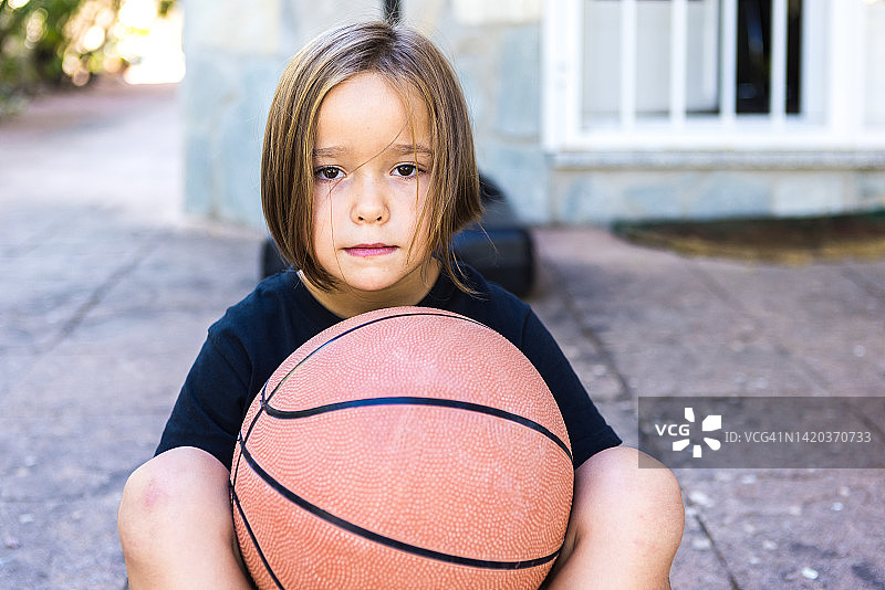 金发女孩的肖像，穿着黑色t恤，拿着篮球，微笑。运动、训练、快乐、健康的生活理念。图片素材