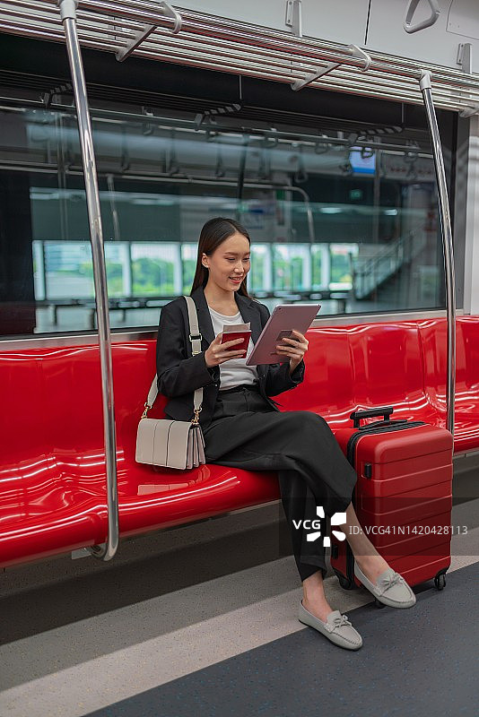 一名年轻的亚洲女商人的肖像照片旅行在通勤火车和红色行李在她的平板电脑上观看视频在旅程过境的商务旅行图片素材