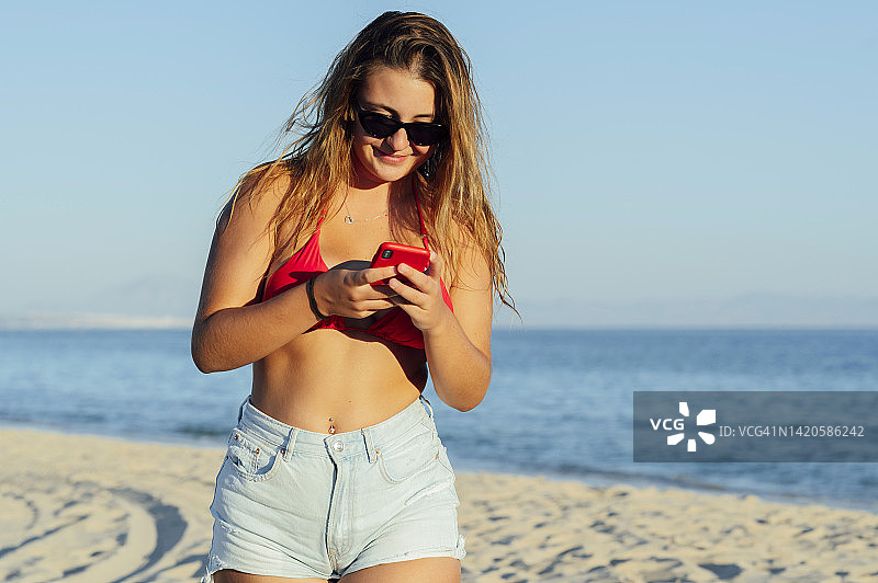 美丽快乐的女人在海滩上用智能手机发短信图片素材