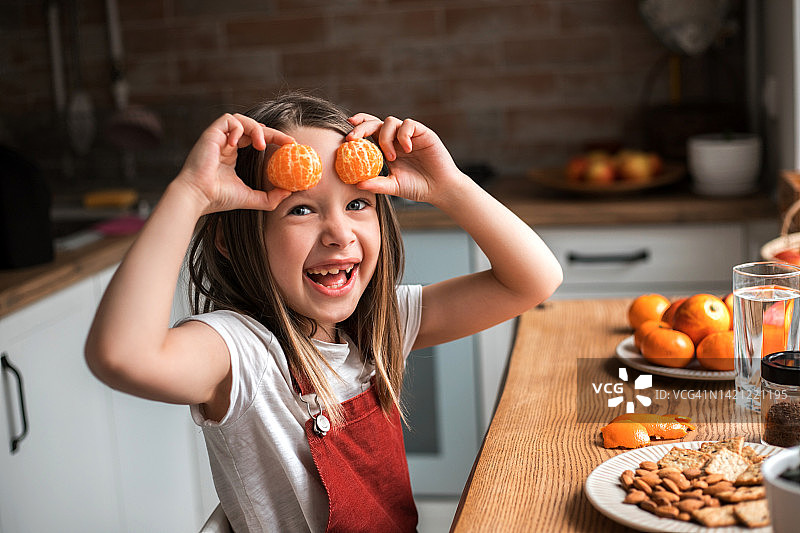 漂亮的小女孩在家里玩橘子。快乐的小女孩带着水果在家里。图片素材
