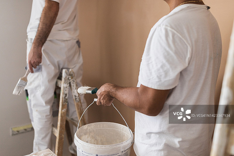 家庭油漆工拿着一桶白色油漆和一个油漆刷图片素材