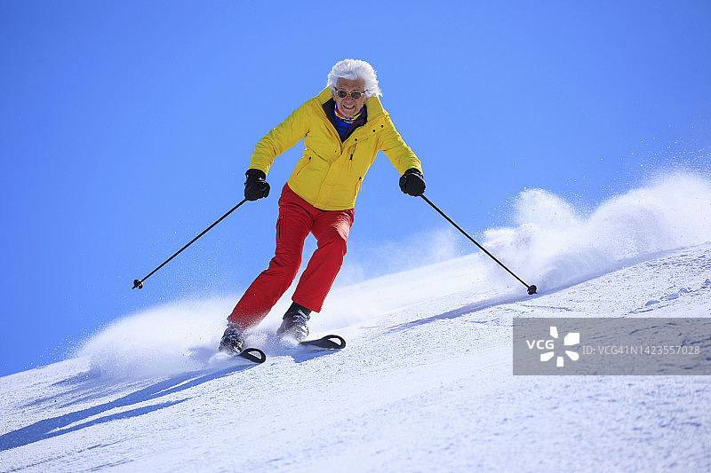 生机勃勃的老人，白发苍苍的男子滑雪，在阳光明媚的滑雪场享受。在蓝天下高速滑雪雕刻。图片素材