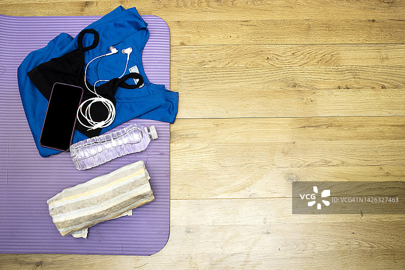 健康的生活方式，运动或运动员装备:一瓶水，耳机，毛巾和衬衫，手机和垫子在木桌上图片素材