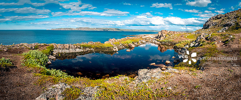 岩石中的天然水池。蓝天白云倒映在清澈的水中。捷里别尔卡附近巴伦支海的岩石海岸线。俄罗斯北部的风景。科拉半岛，摩尔曼斯克州，俄罗斯图片素材