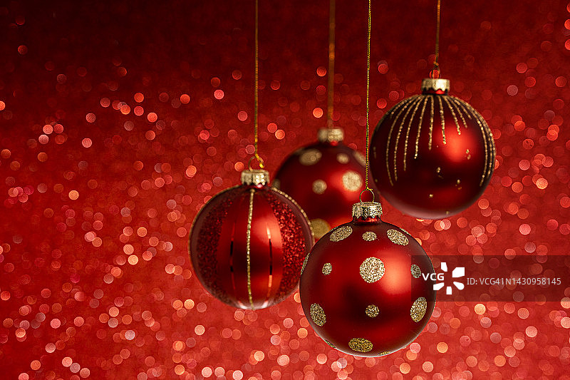 红色的圣诞树球挂在红色的闪闪发光的背景前面。图片素材