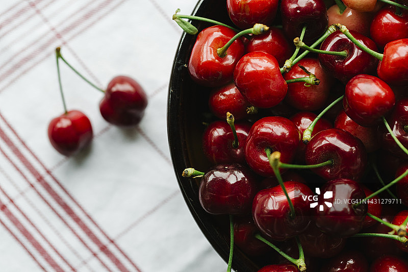 头顶上的新鲜樱桃在陶瓷碗上的红色条纹餐巾-有机水果的概念图片素材