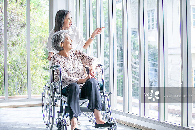 美丽的亚洲女孩帮助和照顾坐在轮椅上的老年妇女在家里的客厅，高级治疗病人在家里的概念。图片素材