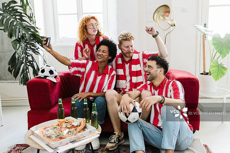 一群年轻的朋友在自拍，看足球比赛，吃着披萨喝着啤酒欢呼，进球后兴高采烈图片素材