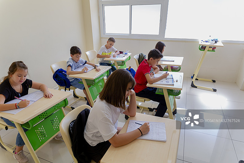 专心致志的小学生坐在课桌前上课，在教室里写字图片素材