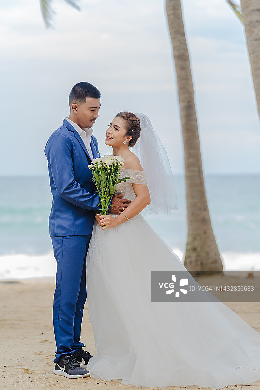 新郎和新娘在海滩上，背景是许多椰子树和大海。图片素材