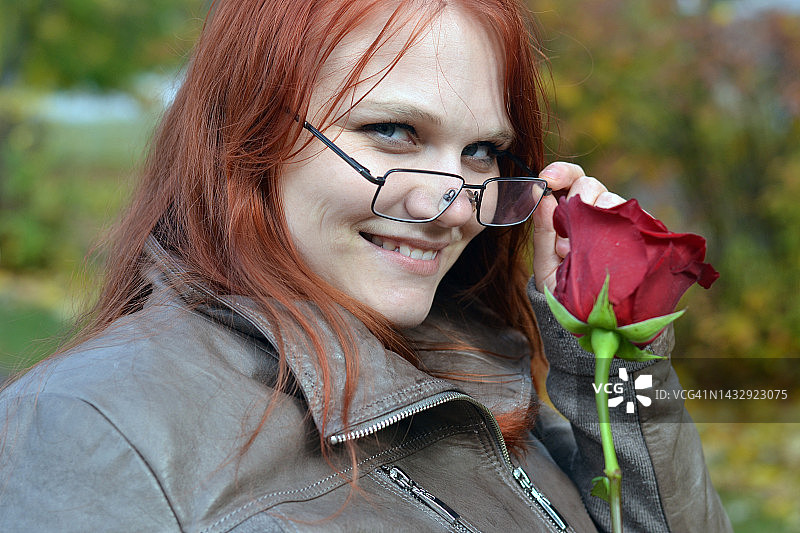戴着红玫瑰的年轻女子在公园里散步。图片素材