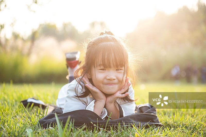 在一个温暖的夏日里，可爱的微笑着的小女孩躺在公园的绿色草地上图片素材