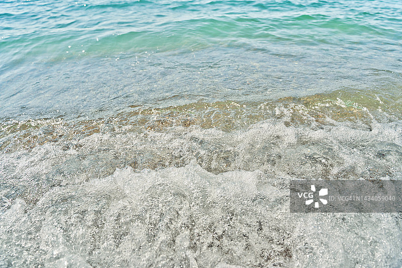 海滩上的白色海浪。蓝绿色的水，自然的背景。图片素材