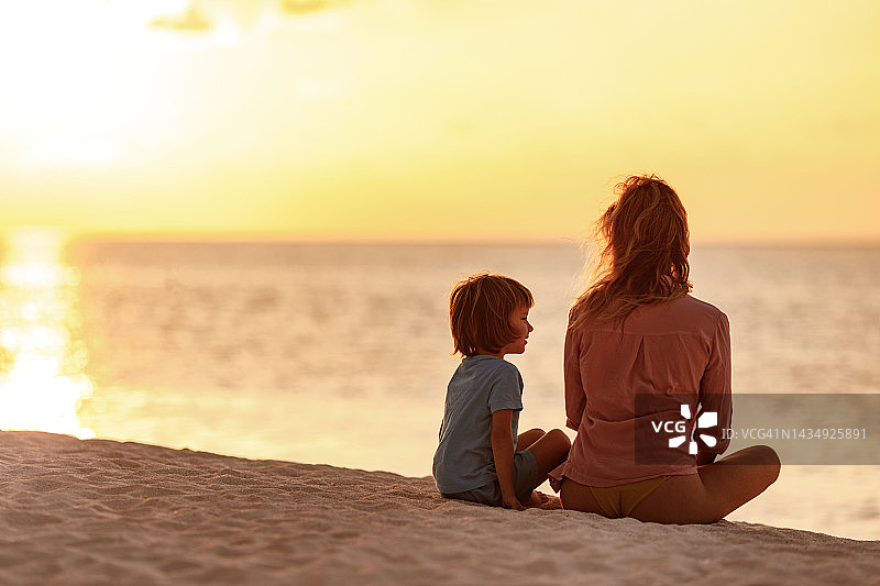 夕阳西下，快乐的男孩和他的单身母亲在海滩上聊天。图片素材