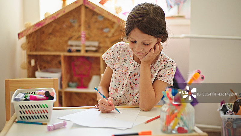 可爱的小女孩在她的桌子上画画图片素材
