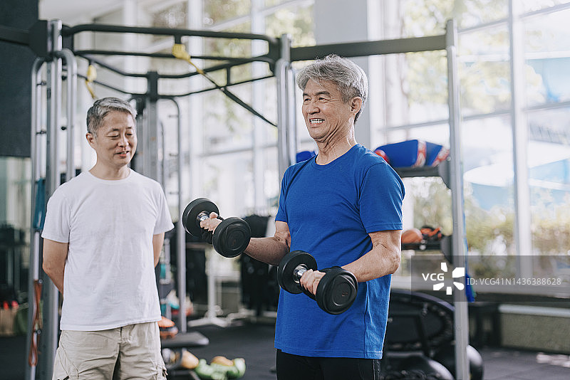 亚裔华人高级私人教练鼓励年长男子在健身房练习哑铃图片素材