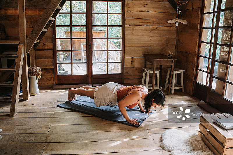一名女子在小木屋里的垫子上练习瑜伽图片素材