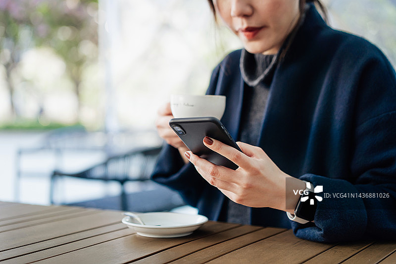 年轻的亚洲女性坐在户外咖啡馆，喝着咖啡，用着智能手机。生活方式和技术图片素材