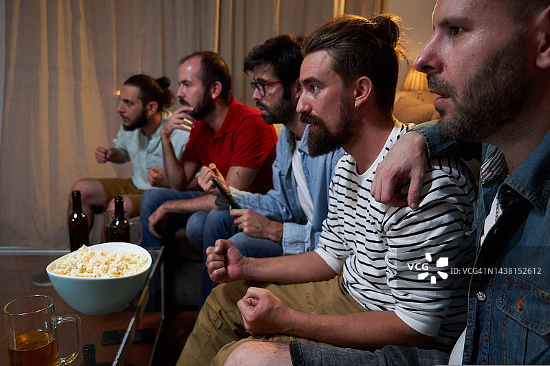 一群男性聚精会神地坐在客厅的沙发上看世界杯足球赛。图片素材