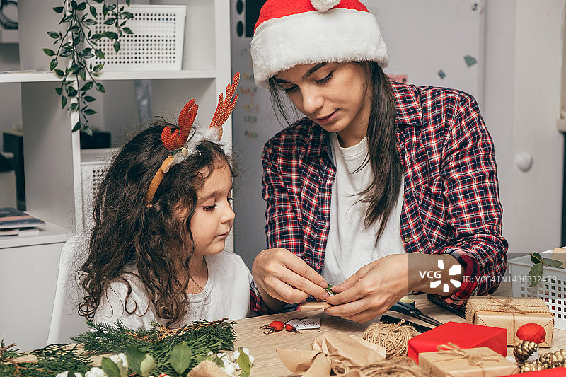 妈妈和小女儿正在家里为圣诞节做准备，包装和装饰礼物。即将到来的假期和庆祝活动图片素材