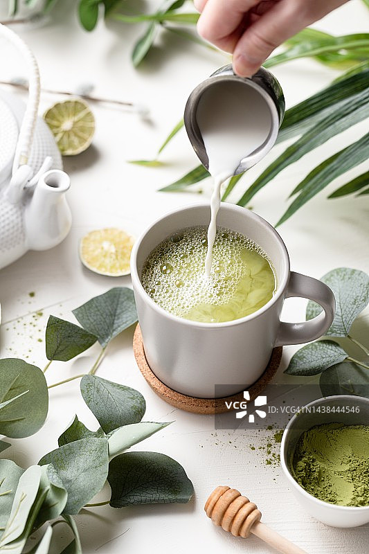 绿茶拿铁，牛奶，白色杯子，绿叶和木勺图片素材