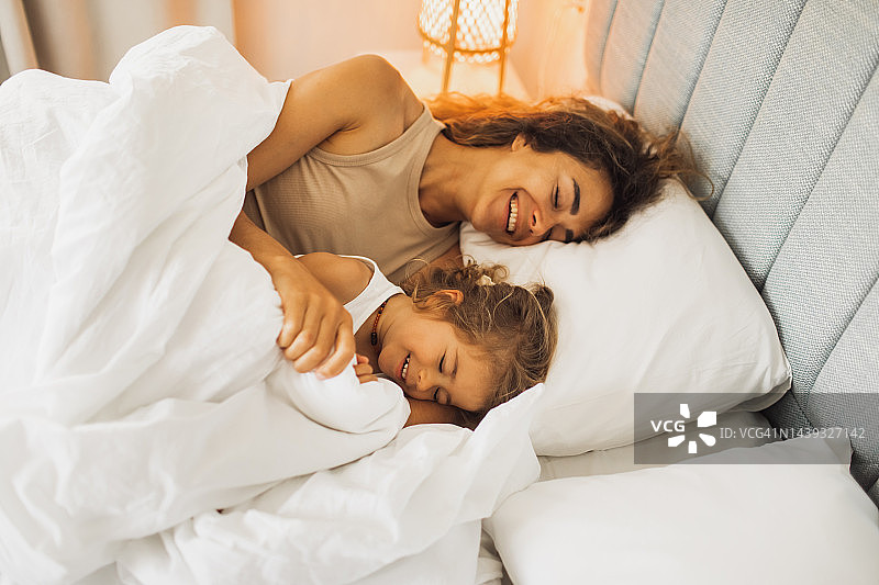 年轻快乐的妈妈和她可爱的小女儿早上在床上玩得很开心。家庭和谐图片素材