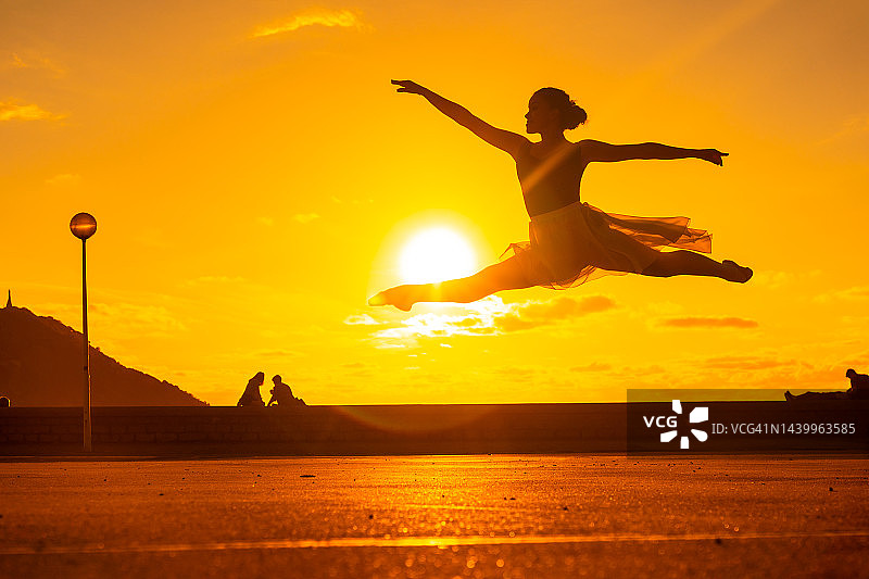 一个年轻的女舞者的剪影在日落时沿着海滩表演跳跃，穿着芭蕾舞裙图片素材