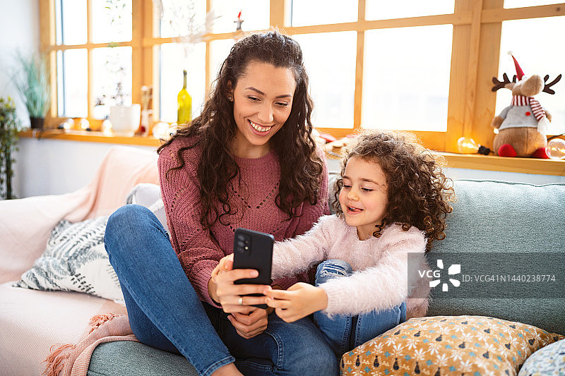 母亲和女儿在视频通话中，在家里享受舒适的圣诞节图片素材