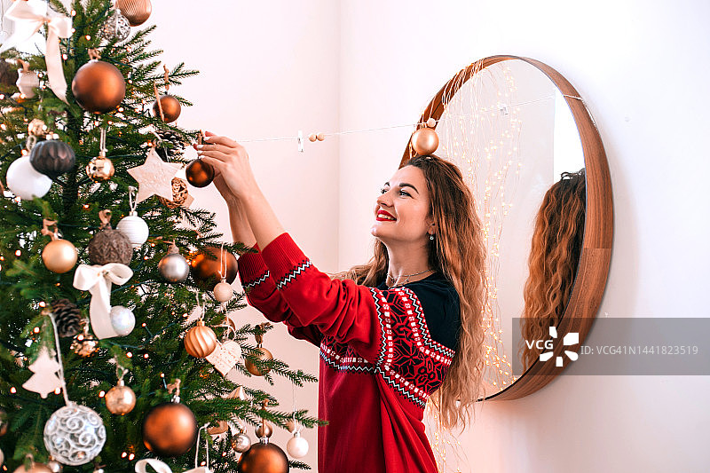 漂亮的成年女子在室内装饰圣诞树。图片素材