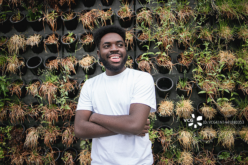 一个快乐的年轻非洲裔美国人在垂直花园前摆姿势的肖像图片素材