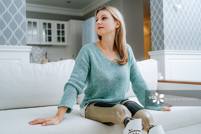 假体的依赖性。放松的金发残疾女性，假腿坐在客厅的沙发上休息图片素材