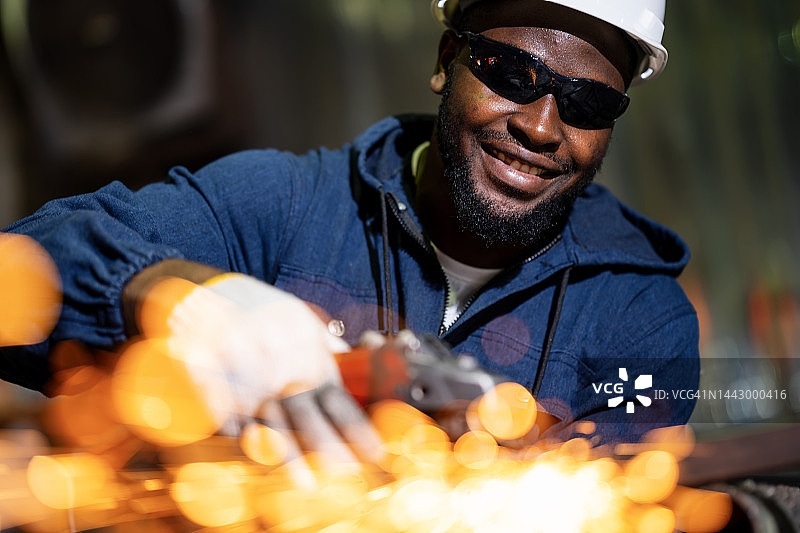 金属加工工业用角磨轮工具。在金属工厂工作的非裔美国男性焊工，同时使用角磨机打磨金属结构框架的焊缝。图片素材