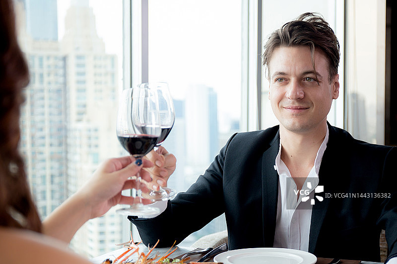 快乐的年轻夫妇端着一杯葡萄酒一起在周年纪念餐厅庆祝，男女约会与浪漫和关系，两个人，情人节和节日的概念。图片素材