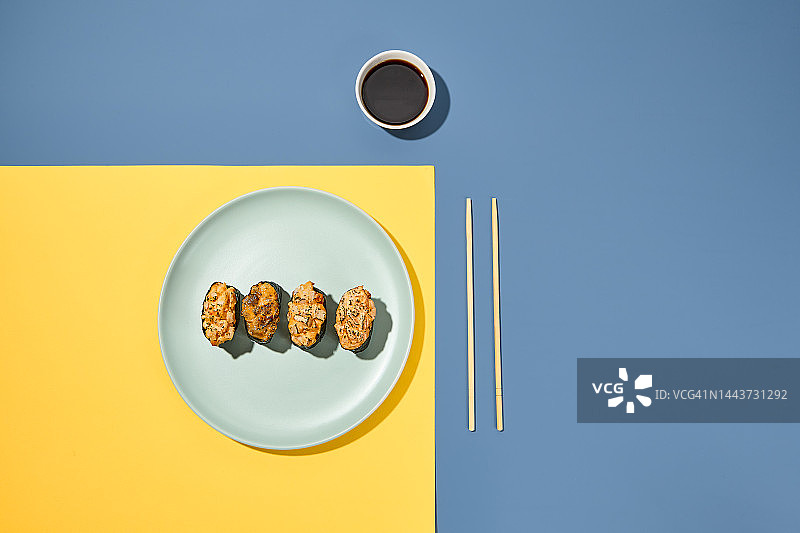 用筷子和酱油装在彩色背景的盘子里。日本食物的最低成分。时尚的概念。Gunkan以充满活力的黄色和蓝色为背景，华丽的食物图片素材