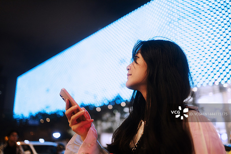 亚洲女商人站在街上的显示屏前使用智能手机图片素材