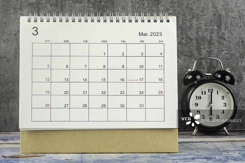 日历桌2023:3月是组织者计划和截止日期的月份，在一个具体背景的桌子上放一个闹钟。图片素材
