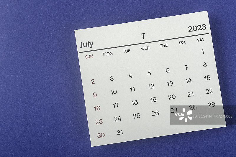 2023年日历桌面的俯视图:7月是组织者用蓝色纸张背景进行计划和截止日期的月份。图片素材