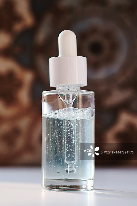 浴室瓷砖背景上的一瓶透明美容精华液。图片素材