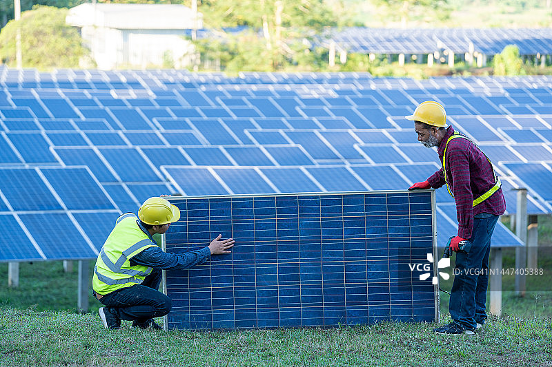 在太阳能发电厂更换太阳能电池板的工程师或电工。图片素材