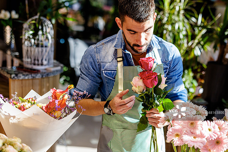 在花店里，一名男工人正捧着鲜花，享受着芬芳。图片素材