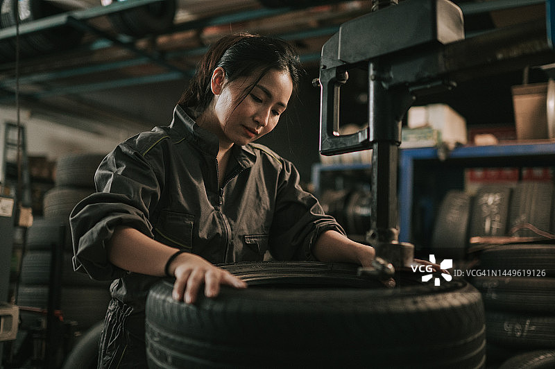 图为女机械师在汽车修理厂用机器更换轮胎图片素材