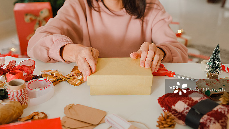 特写的妇女手包装圣诞礼物盒在家里的桌子上。图片素材