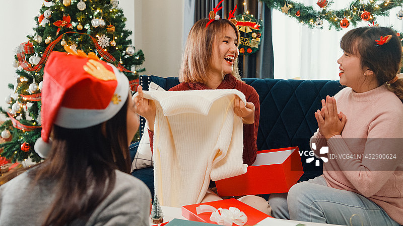 一群年轻的亚洲朋友在家里客厅的沙发上打开圣诞礼物。图片素材