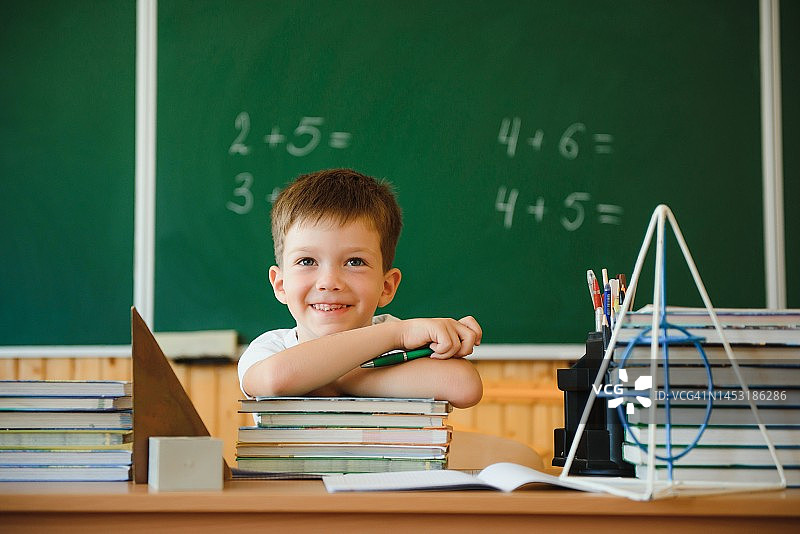 回到学校。在学校的黑板背景上，一名学生第一次坐在桌前看书。图片素材