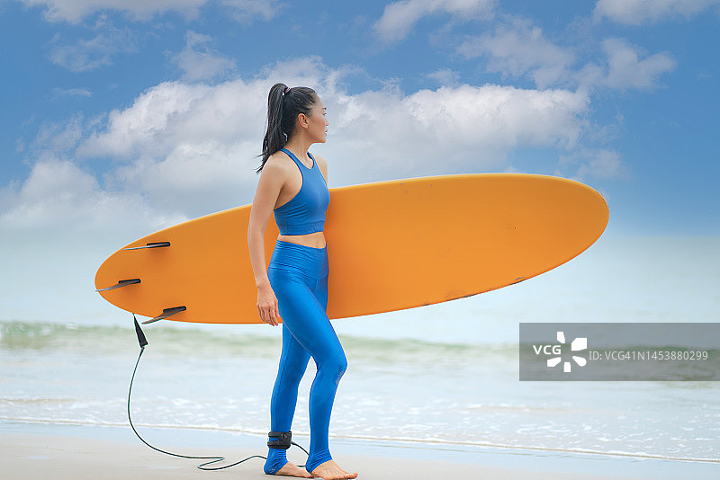 亚洲女子冲浪者享受夏天与冲浪板在海滩上。图片素材