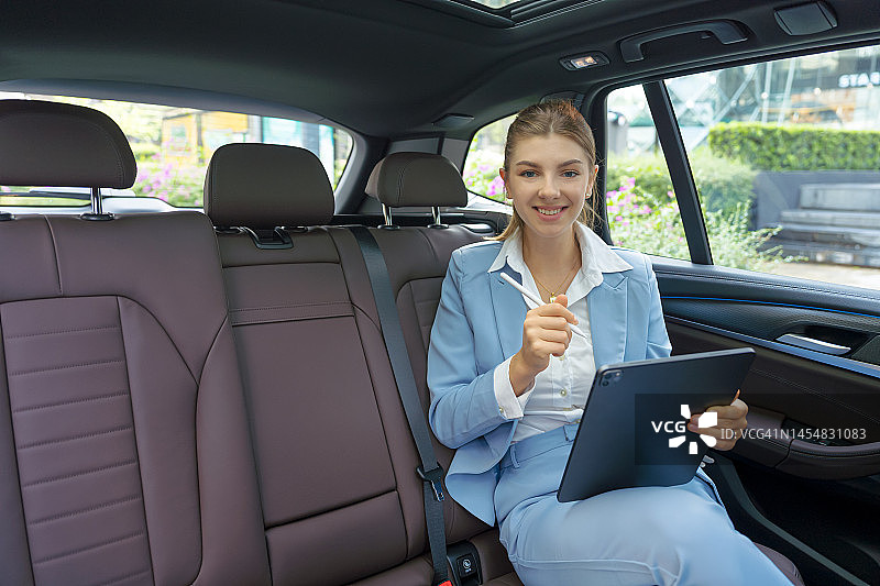 女商人正在开车旅行。她正坐在后座上摆弄平板电脑。图片素材