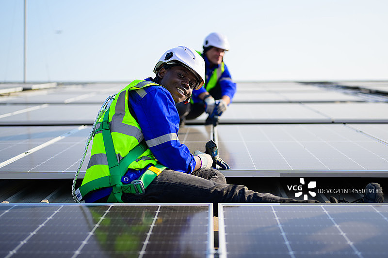 在工厂屋顶安装太阳能电池板的专业技术人员，太阳能电池农场发电厂的工人检查和操作系统，电力和动力的可再生能源，太阳能电池维护概念图片素材