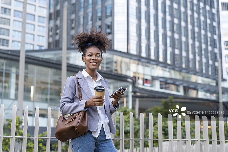 现代年轻女子走在城市的街道上发短信，拿着一杯咖啡图片素材