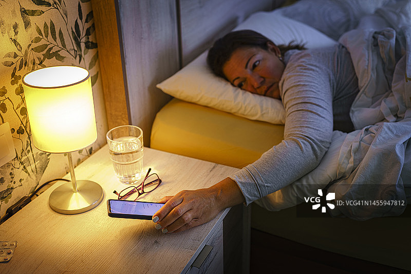 一名女子在睡觉时查看智能手机时间图片素材