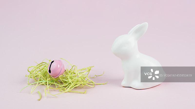 复活节兔子或小白兔，窝里有绿草和铃铛，春节贺卡，粉色粉彩，色彩简约图片素材
